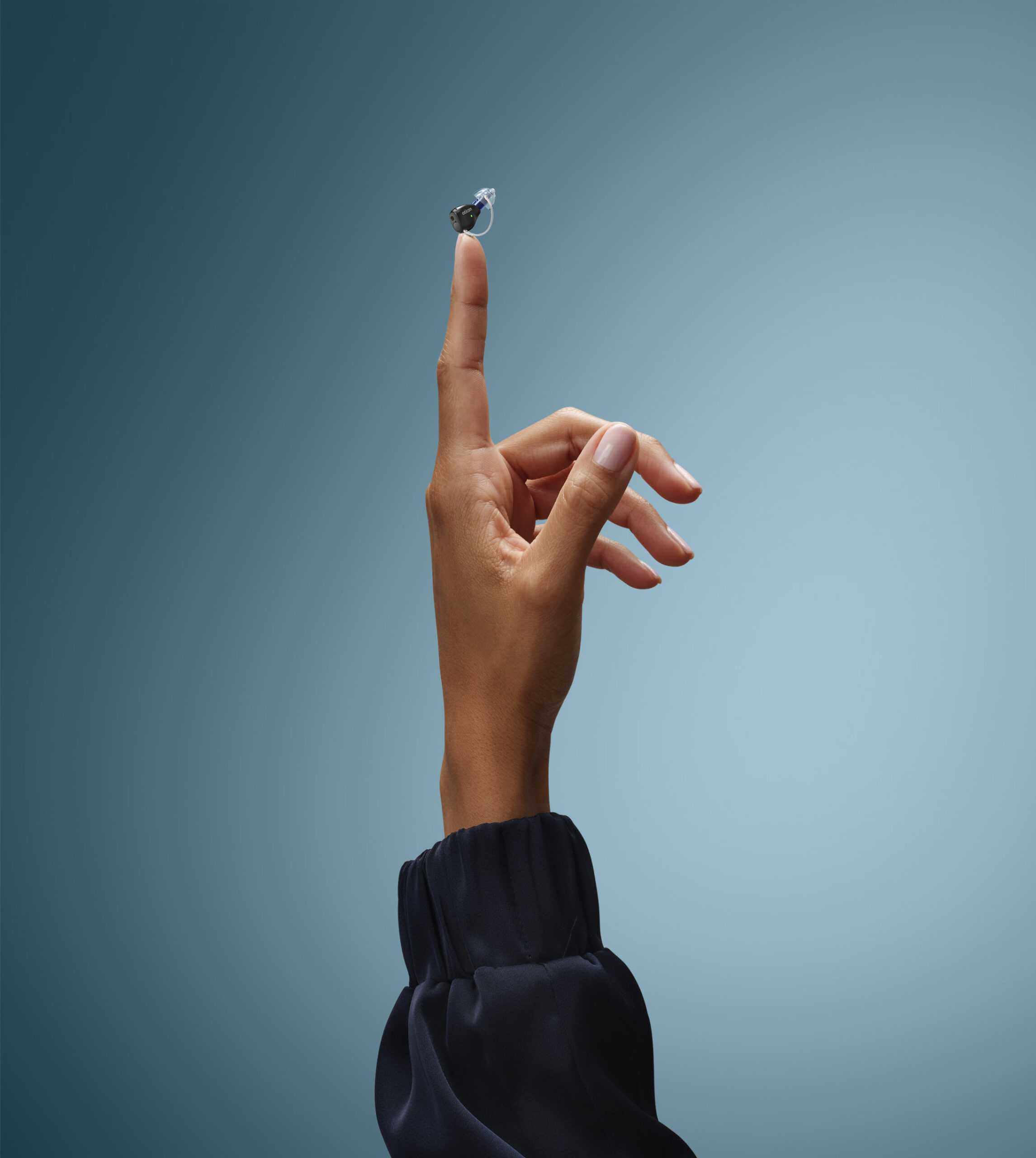 Oticon_Zeal_Product_on_Finger_Steel_blue_Background_KC_25_2_4848_Vertical